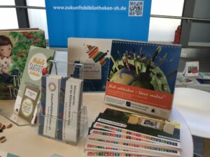 Tisch mit Flyern und Infomaterialien der Zukunftsbibliotheken SH, Informationen zur mobilen Saatgutbibliothek und ein Kalender der Büchereizentrale Schleswig-Holstein zur Agenda 2030